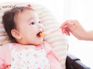 イメージ写真_スプーンでご飯を食べさせてもらっている乳幼児